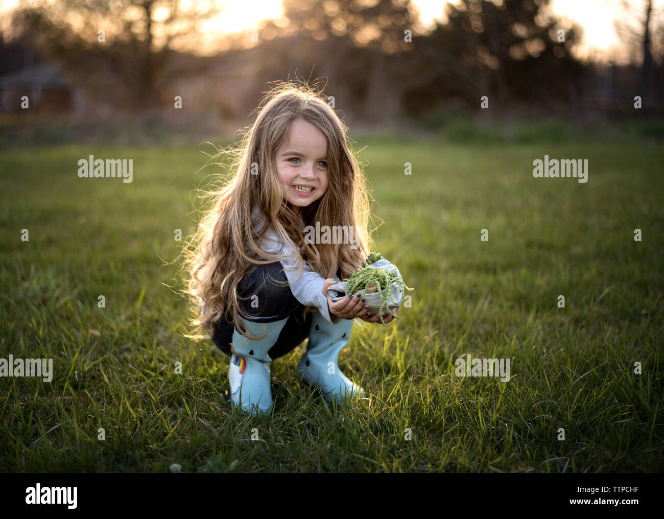 Happy young girl wearing rain boots et holding green plant Banque D'Images
