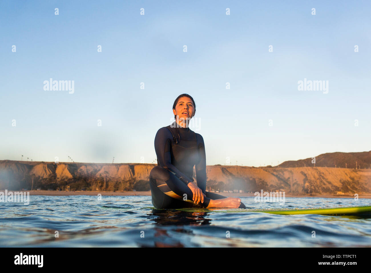 Jeune femme assise sur une planche de surf en mer contre ciel clair Banque D'Images