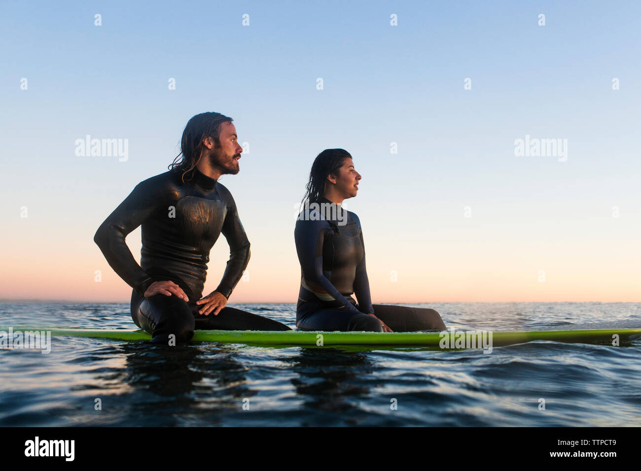 Young couple relaxing on surfboards en mer pendant le coucher du soleil Banque D'Images