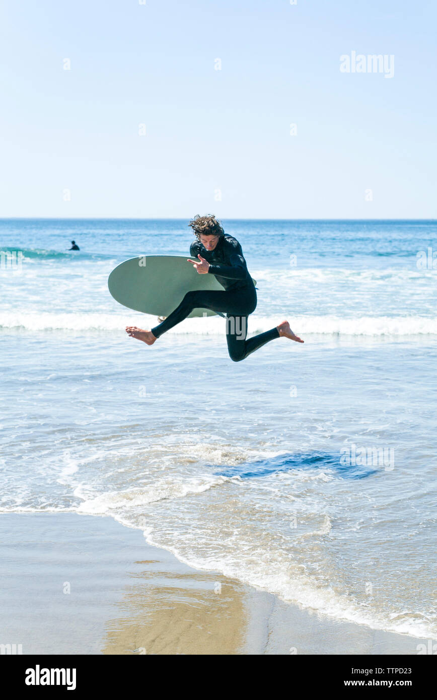 Man with surfboard sauter en mer contre ciel clair Banque D'Images