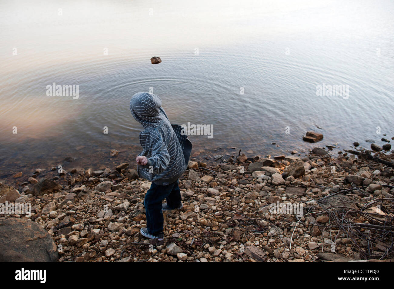 Vue latérale du boy wearing hooded shirt jeter dans le lac de pierre Banque D'Images