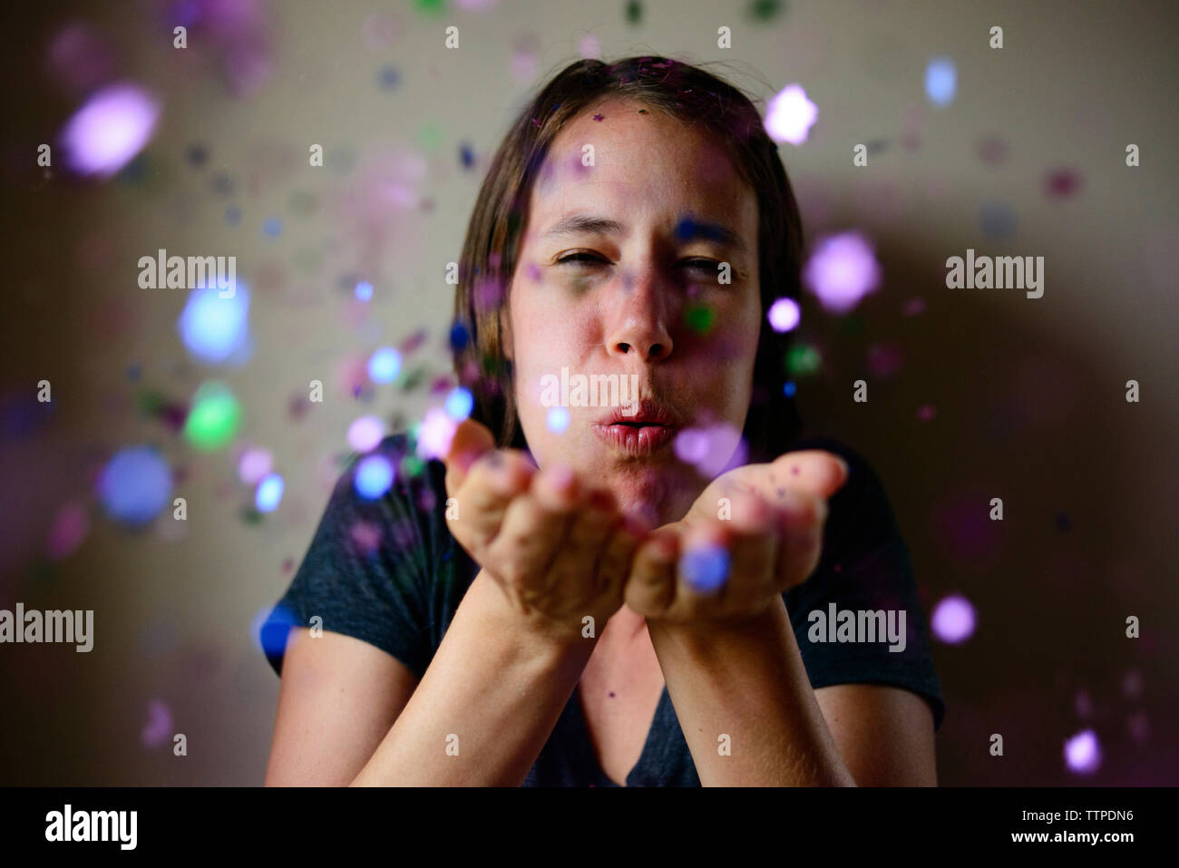 Woman blowing confetti contre mur Banque D'Images