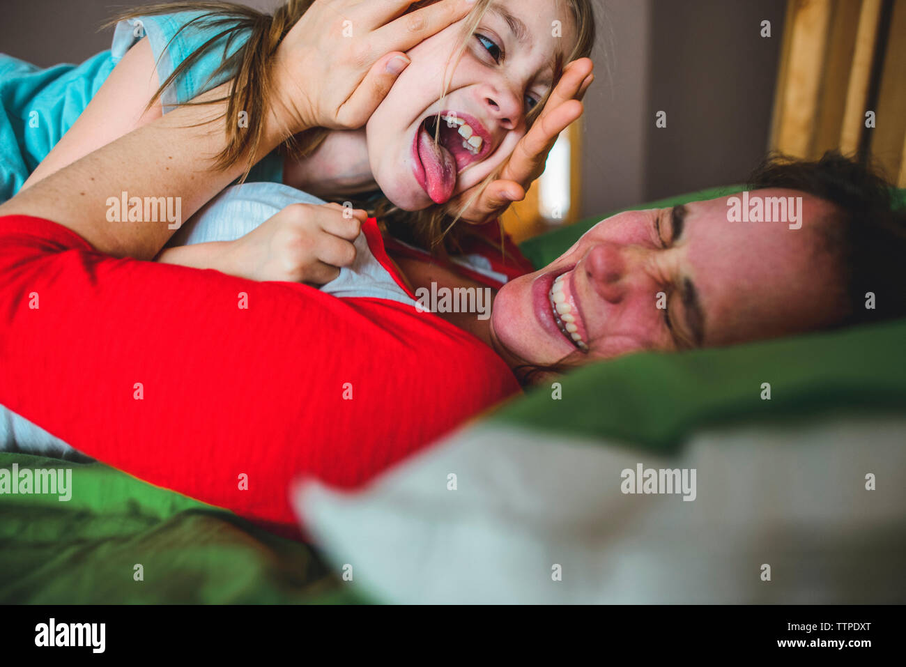 Vue de côté fille espiègle licking mother lying on bed at home Banque D'Images