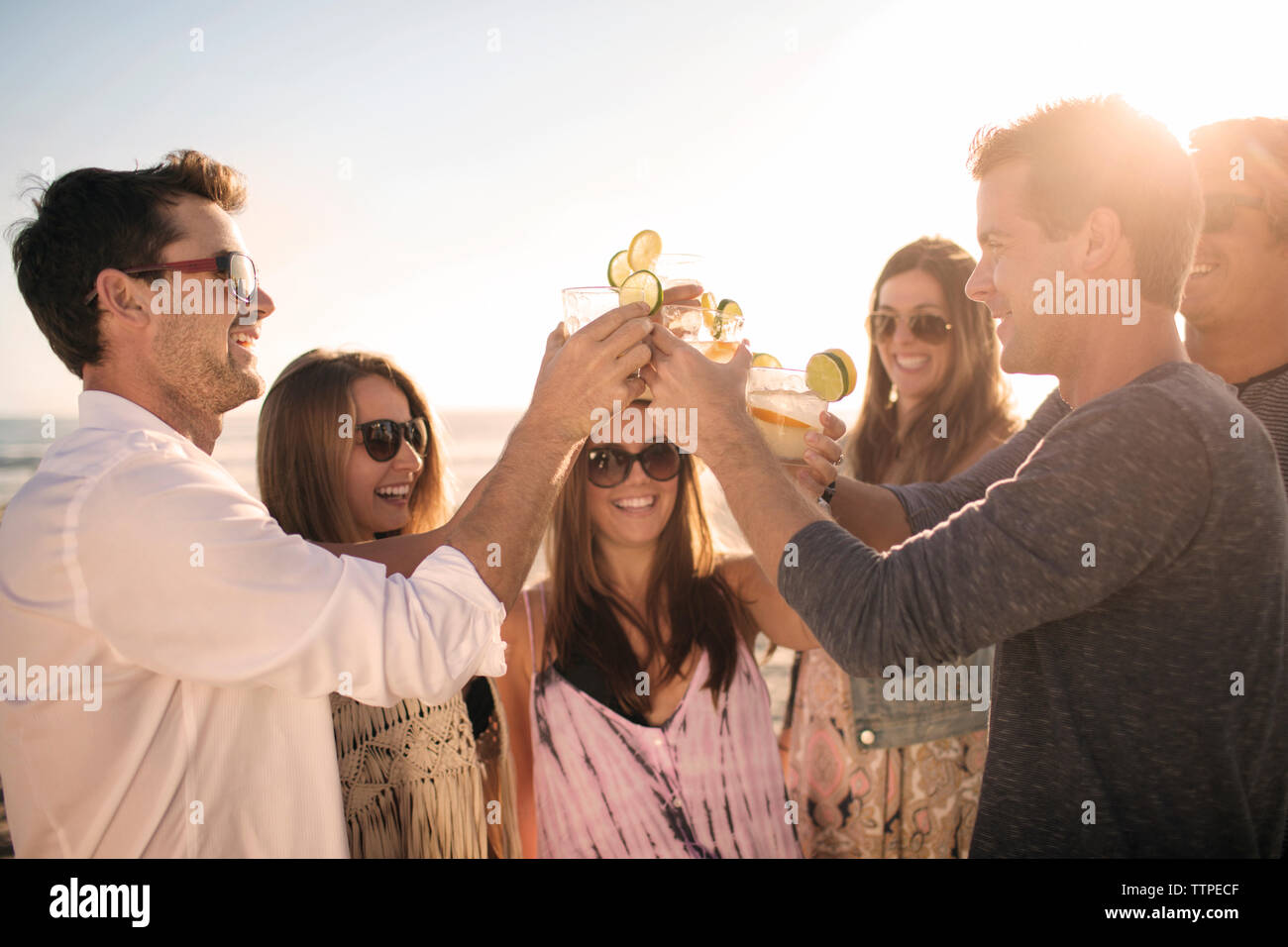 Cheerful friends toasting drinks sur la plage pendant le coucher du soleil Banque D'Images