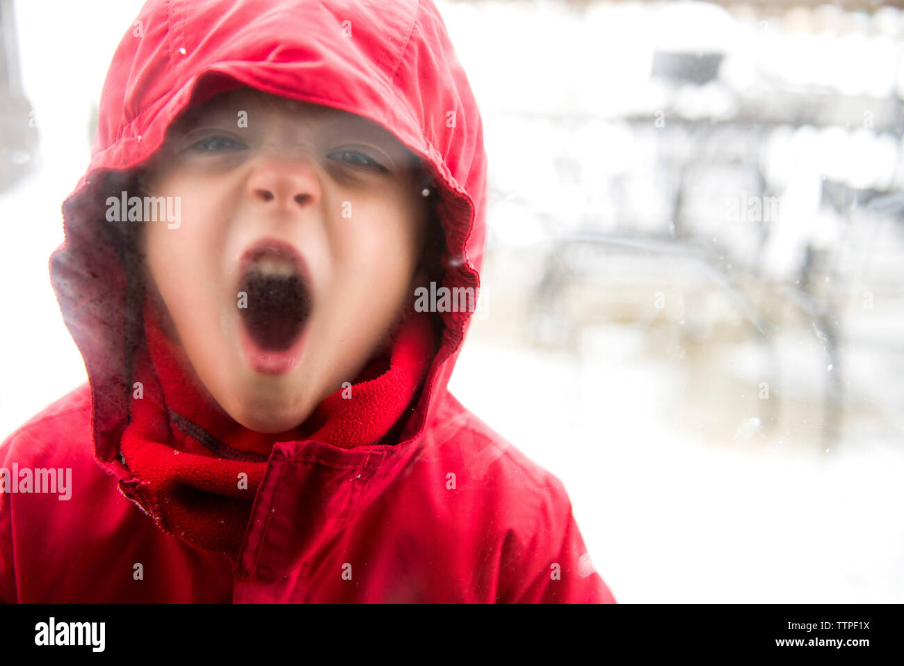 Portrait of playful boy wearing vêtements chauds alors que la fenêtre de buée avec la vapeur d'haleine Banque D'Images