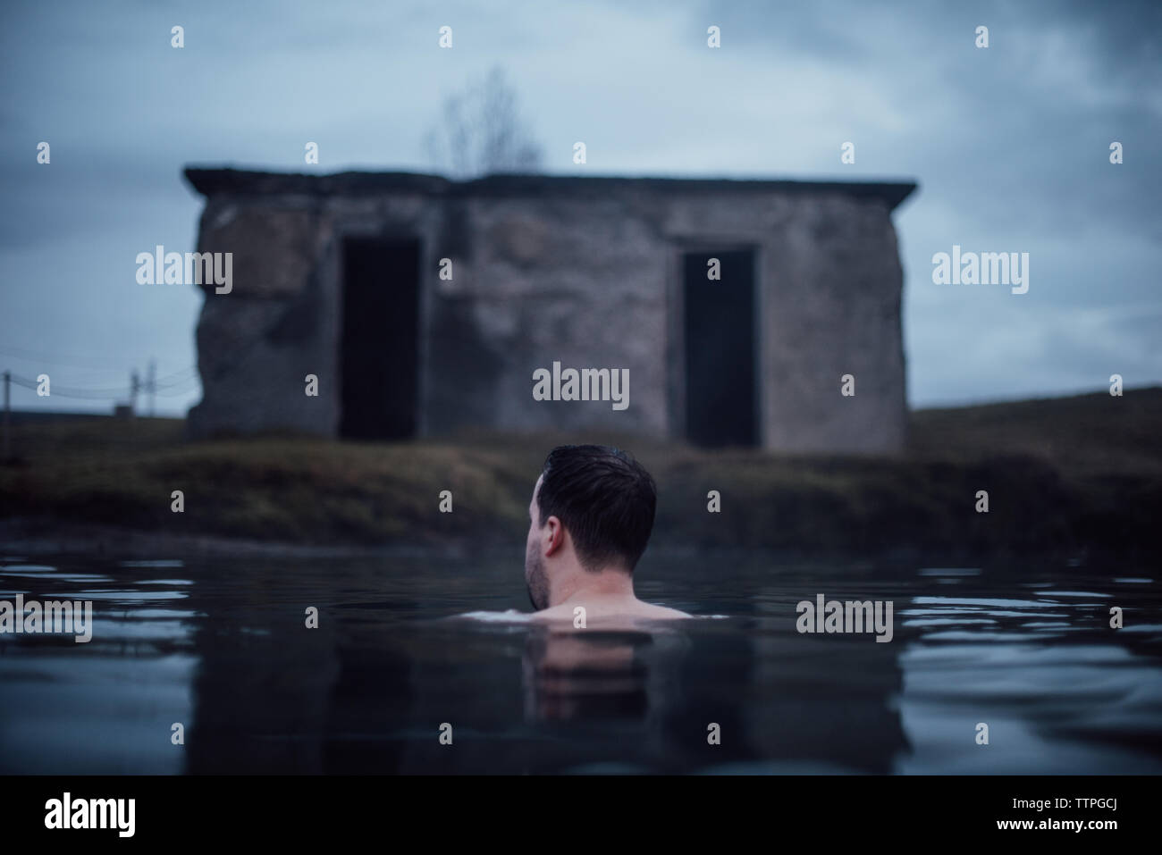 Homme Natation en Secret Lagoon en Islande avec cabine abandonnée Banque D'Images