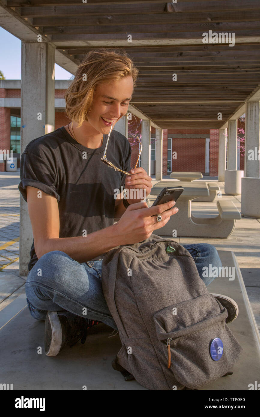 Male student sitting en souriant au téléphone message Banque D'Images