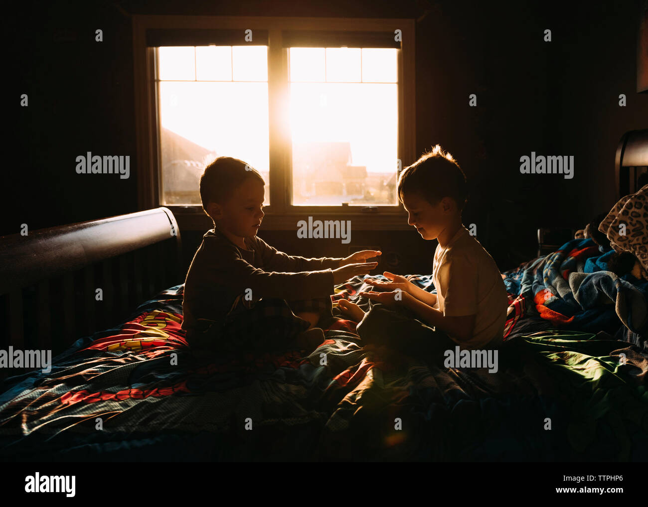 Frères jouant alors qu'assis sur le lit contre fenêtre dans darkroom Banque D'Images