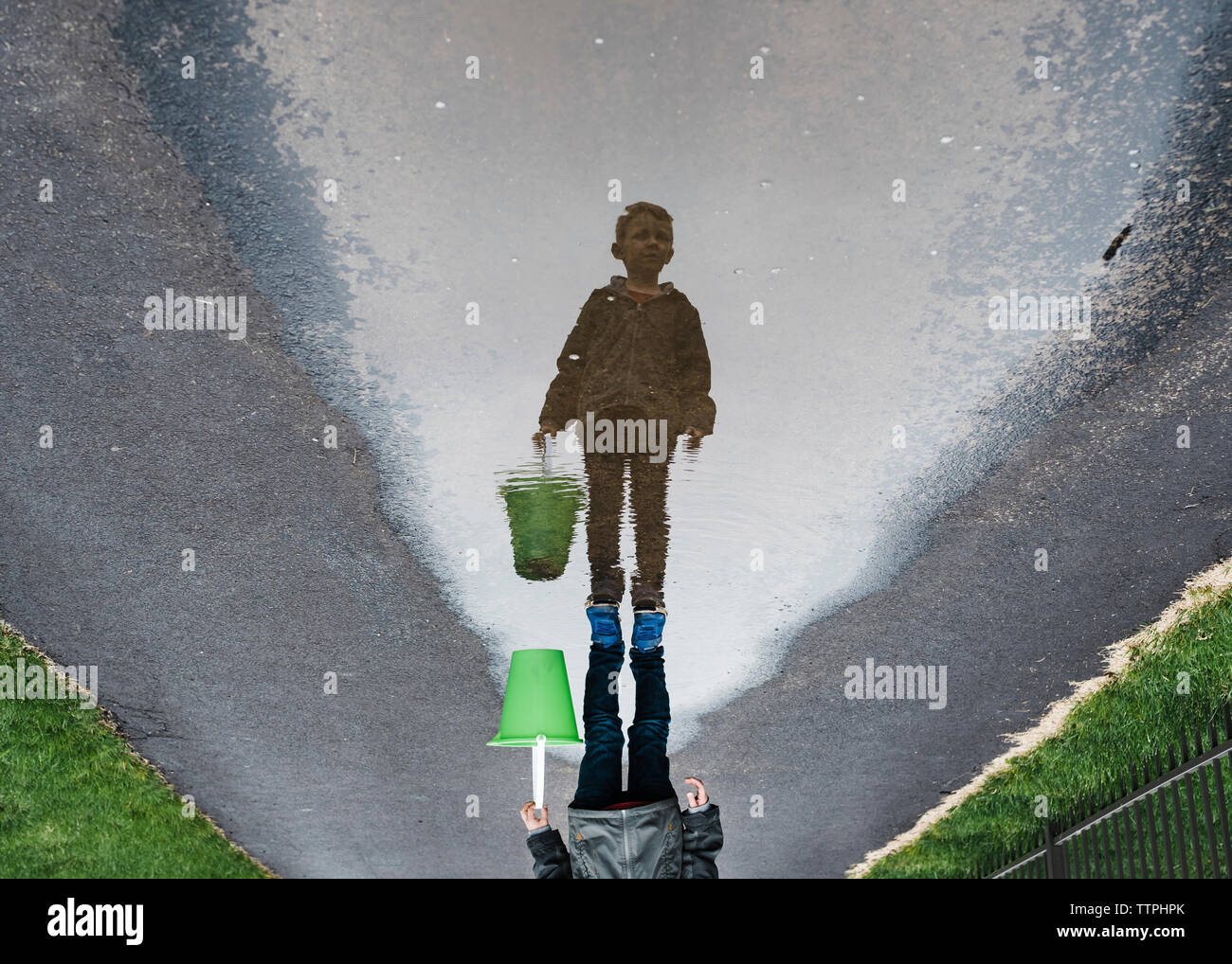 L'envers de l'image garçon debout sur route mouillée en transportant le godet Banque D'Images