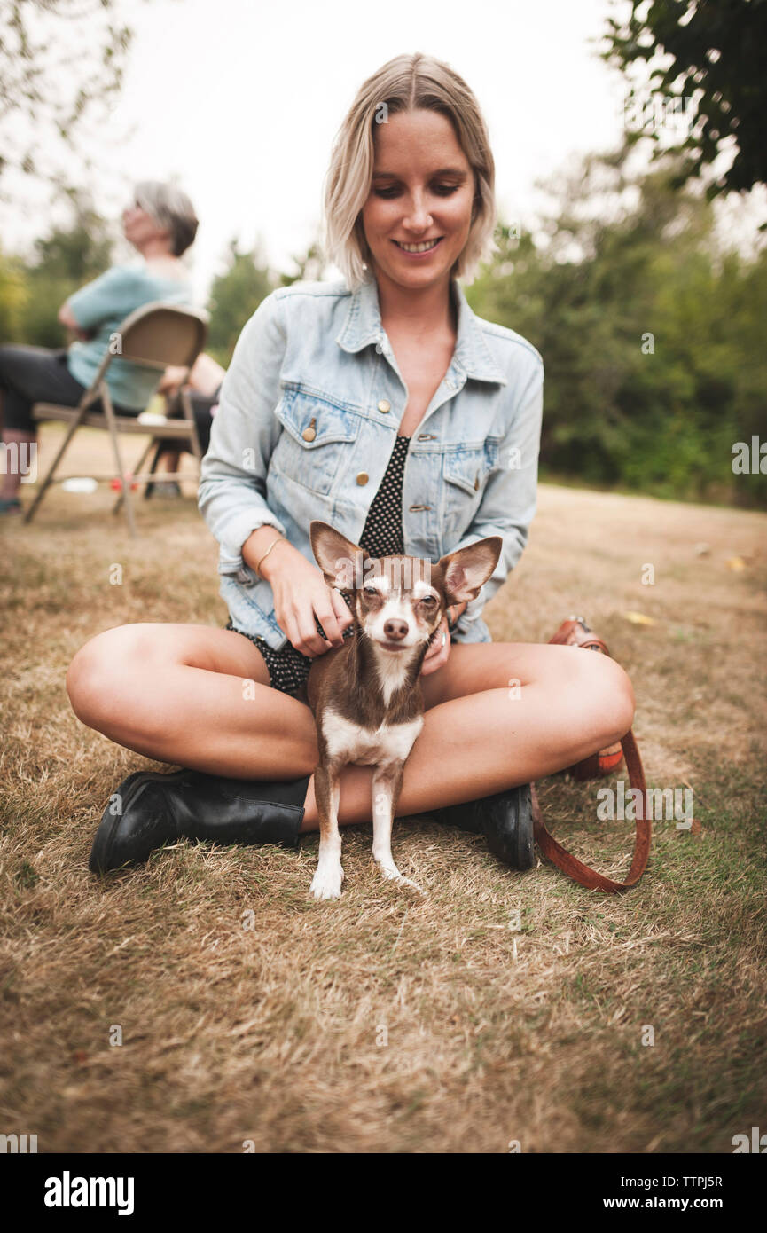 Smiling woman Playing with Chihuahua while sitting on grassy field in yard Banque D'Images