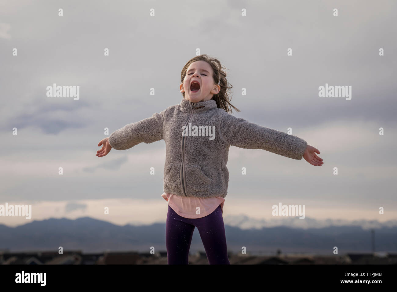 Happy girl with arms outstretched hurlant debout contre ciel nuageux Banque D'Images