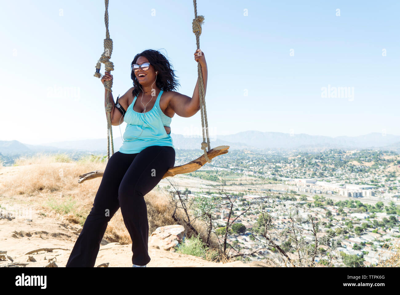 Happy woman swinging sur rope swing contre townscape Banque D'Images
