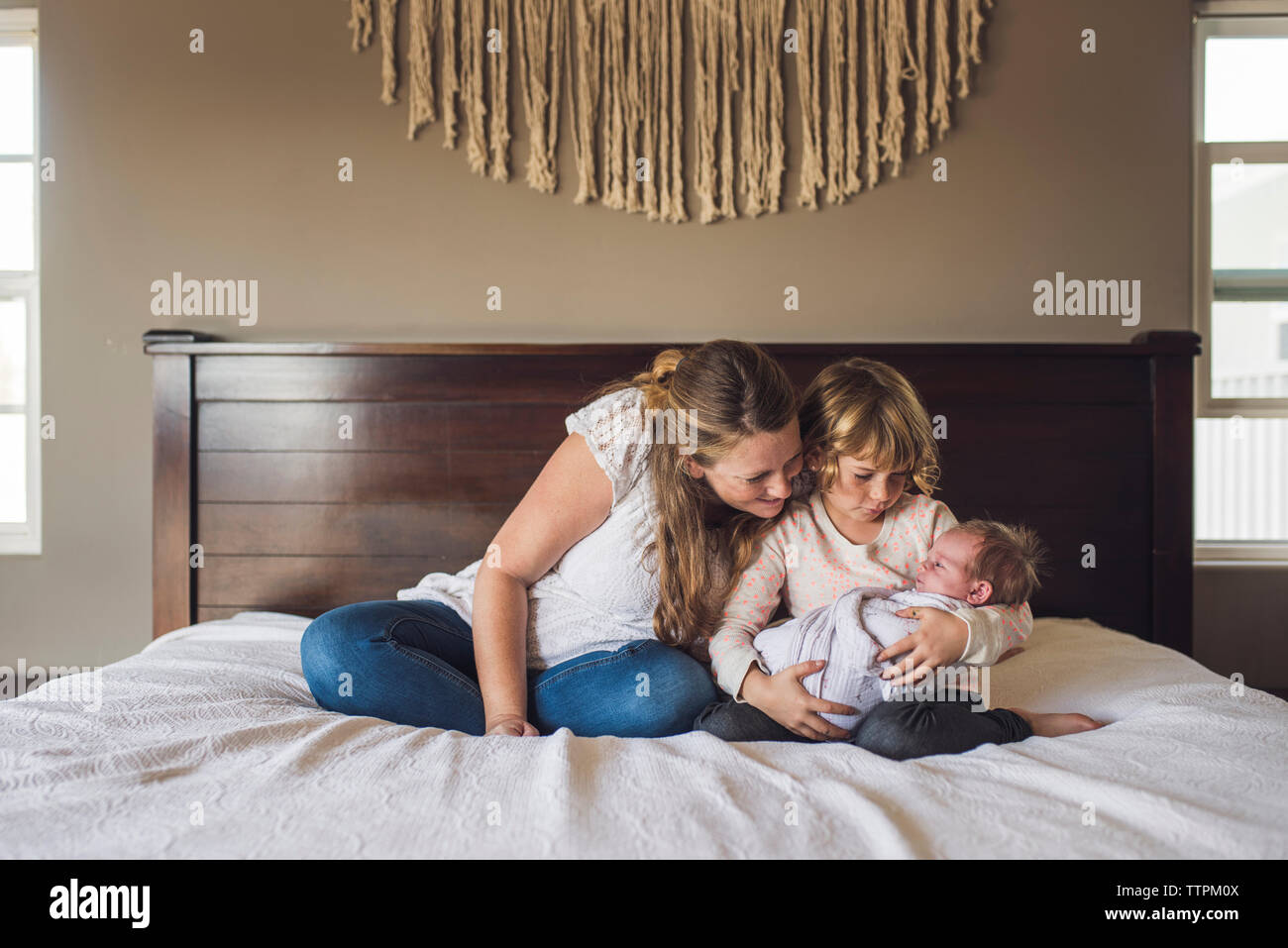 Mère regardant bébé fille porté par sa fille sur le lit chez lui Banque D'Images