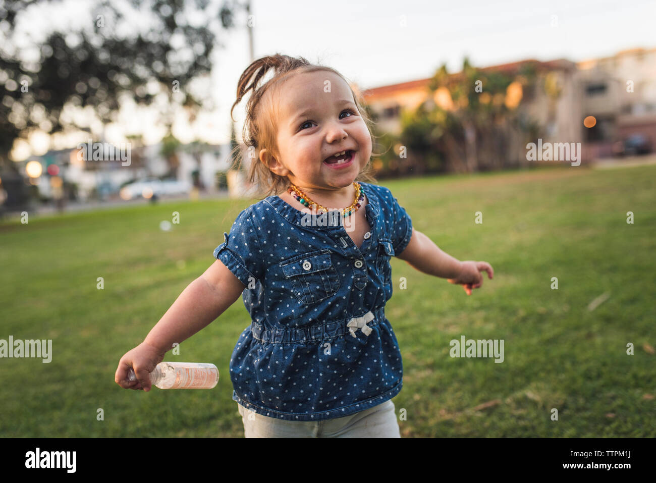 Happy baby girl looking away while standing on grassy field contre sky at park Banque D'Images