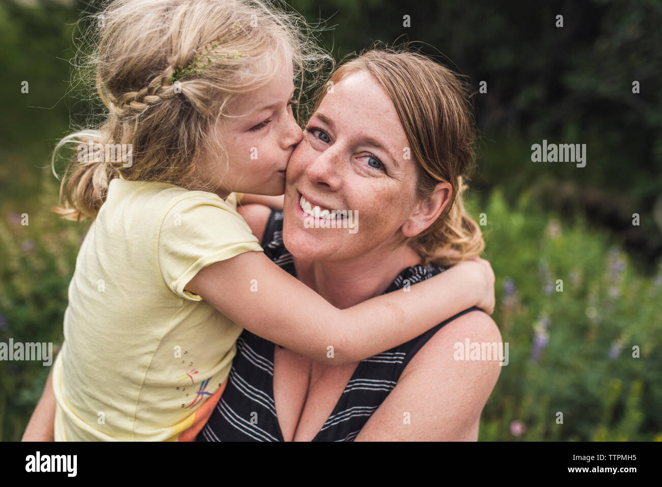 Vue latérale du baiser fille mère debout sur terrain en forêt Banque D'Images