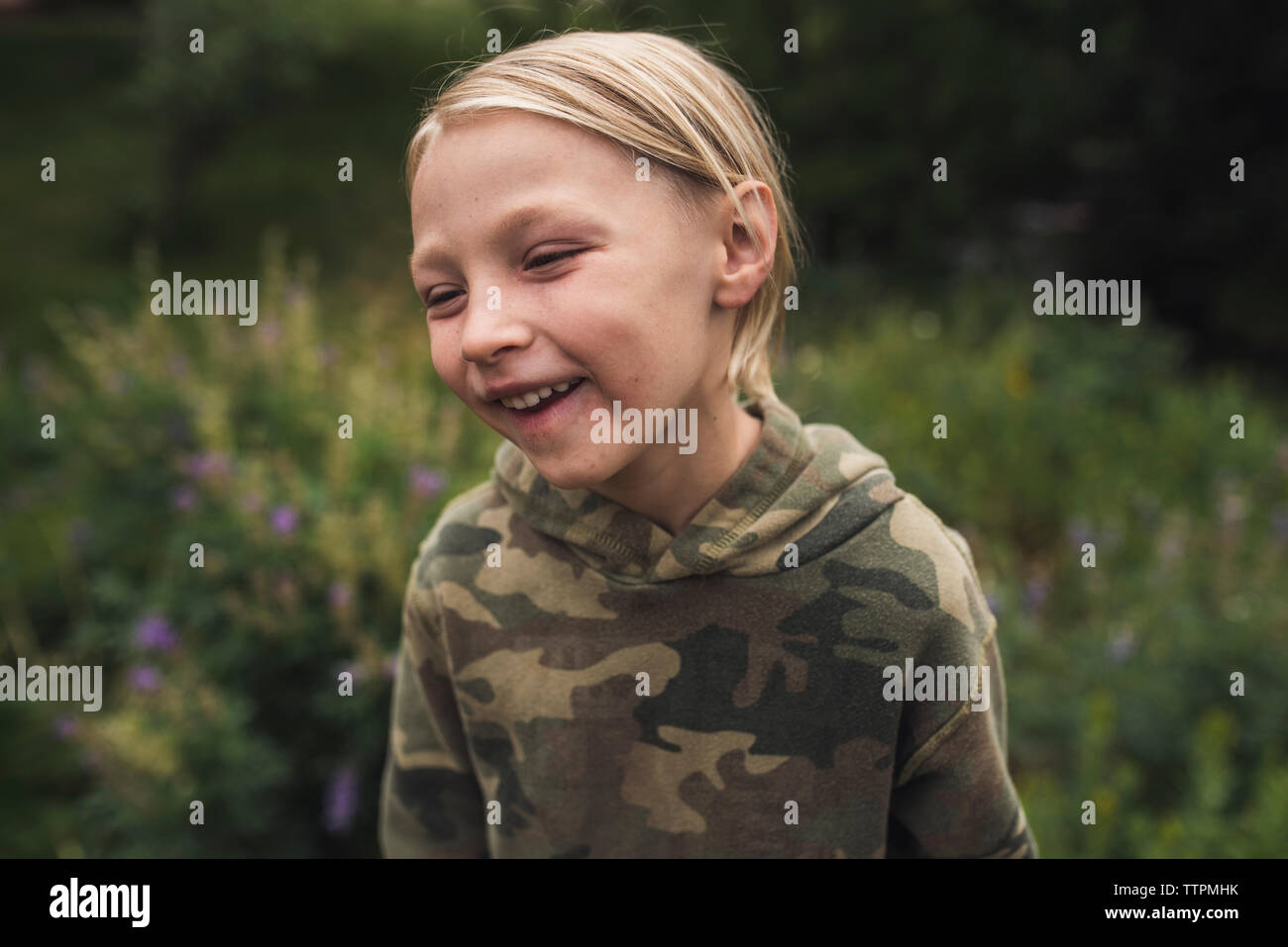 Close-up of happy boy aux cheveux blonds à l'écart en se tenant sur le terrain herbeux en forêt Banque D'Images