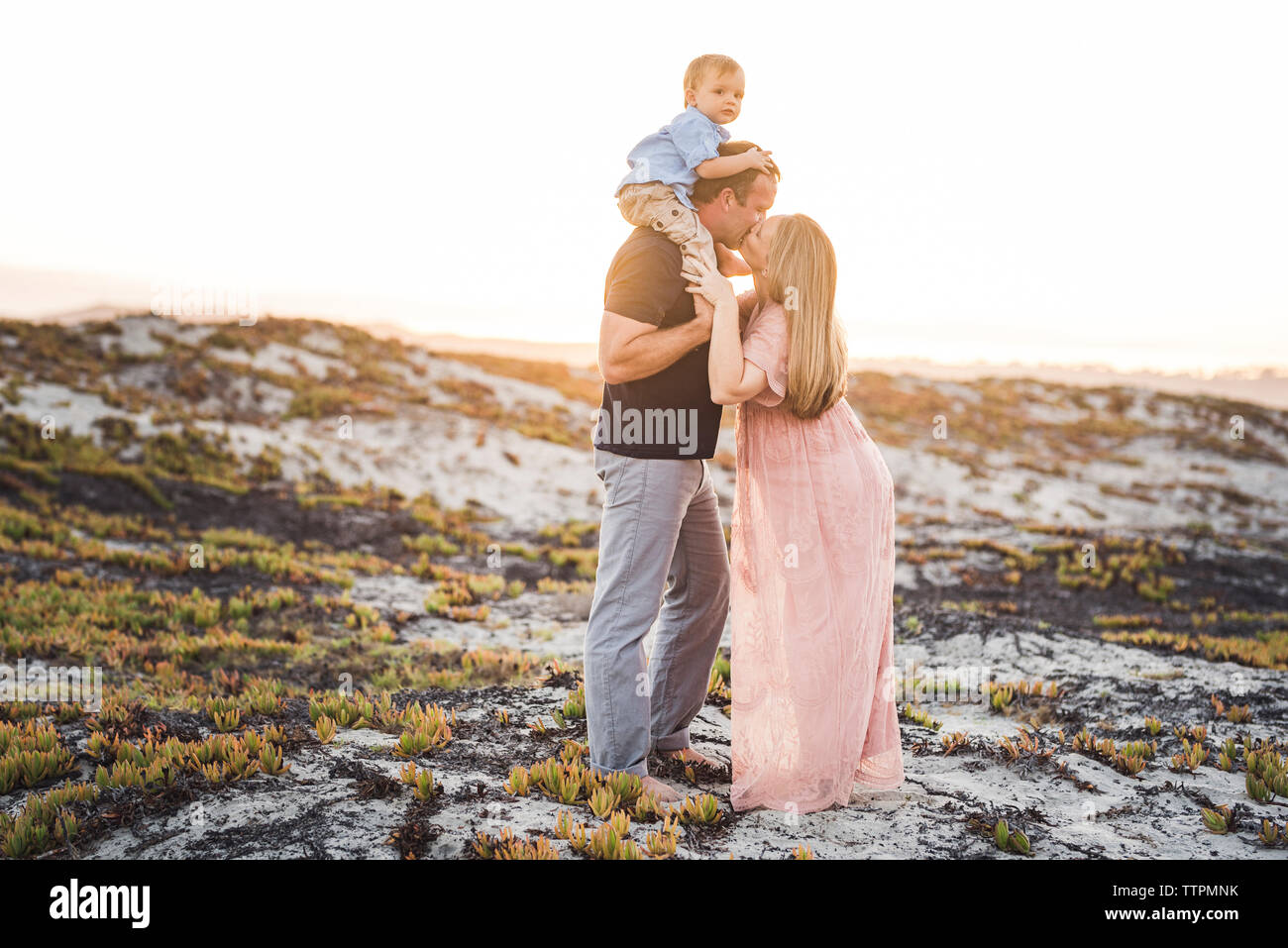 Mari Femme embrasser tout en portant son on shoulders at beach against clear sky pendant le coucher du soleil Banque D'Images