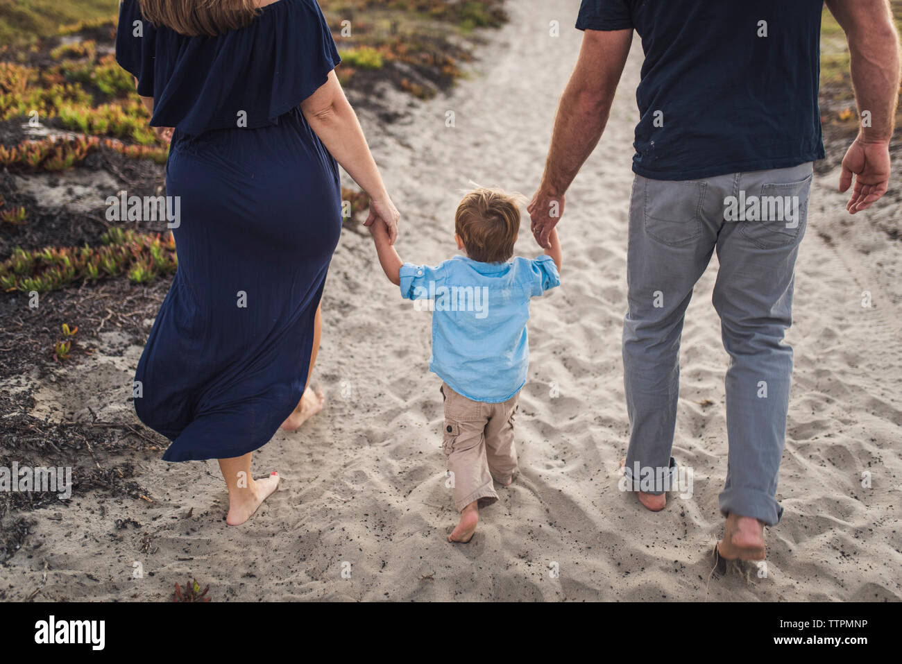 La section basse des parents tenant les mains de son fils tout en marchant sur le sable à la plage pendant le coucher du soleil Banque D'Images