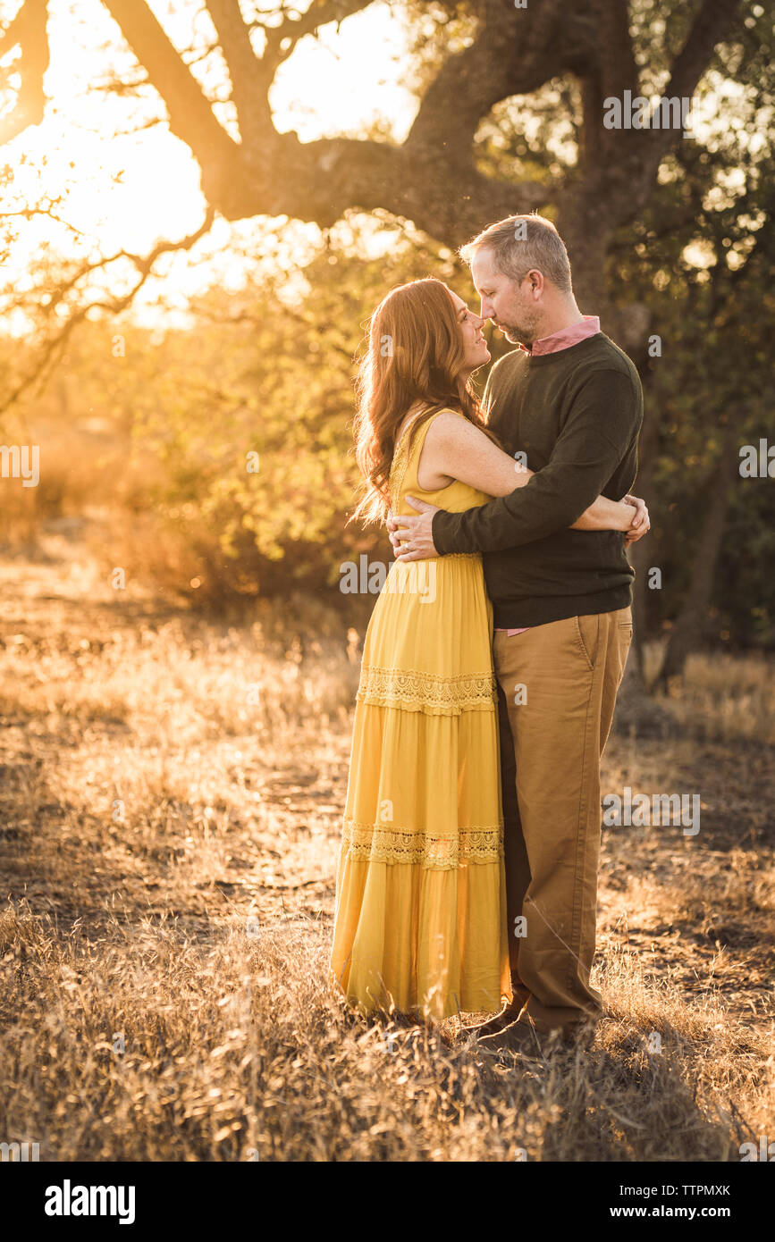 Woman embracing mari alors qu'en Californie pendant le coucher du soleil sur le terrain Banque D'Images