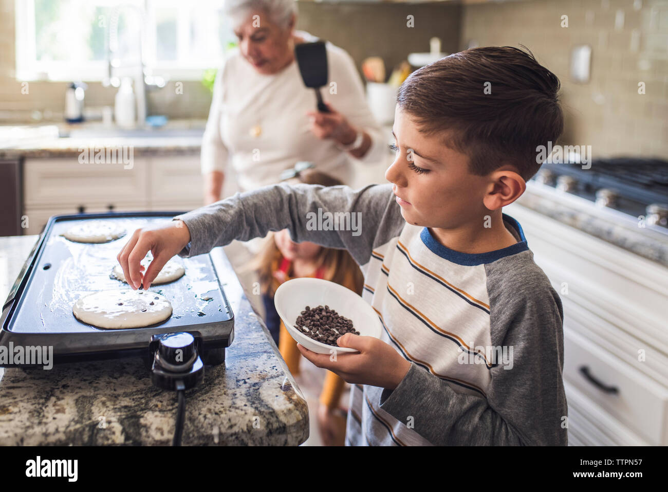Jeune garçon la cuisson des crêpes avec famille de plusieurs générations Banque D'Images