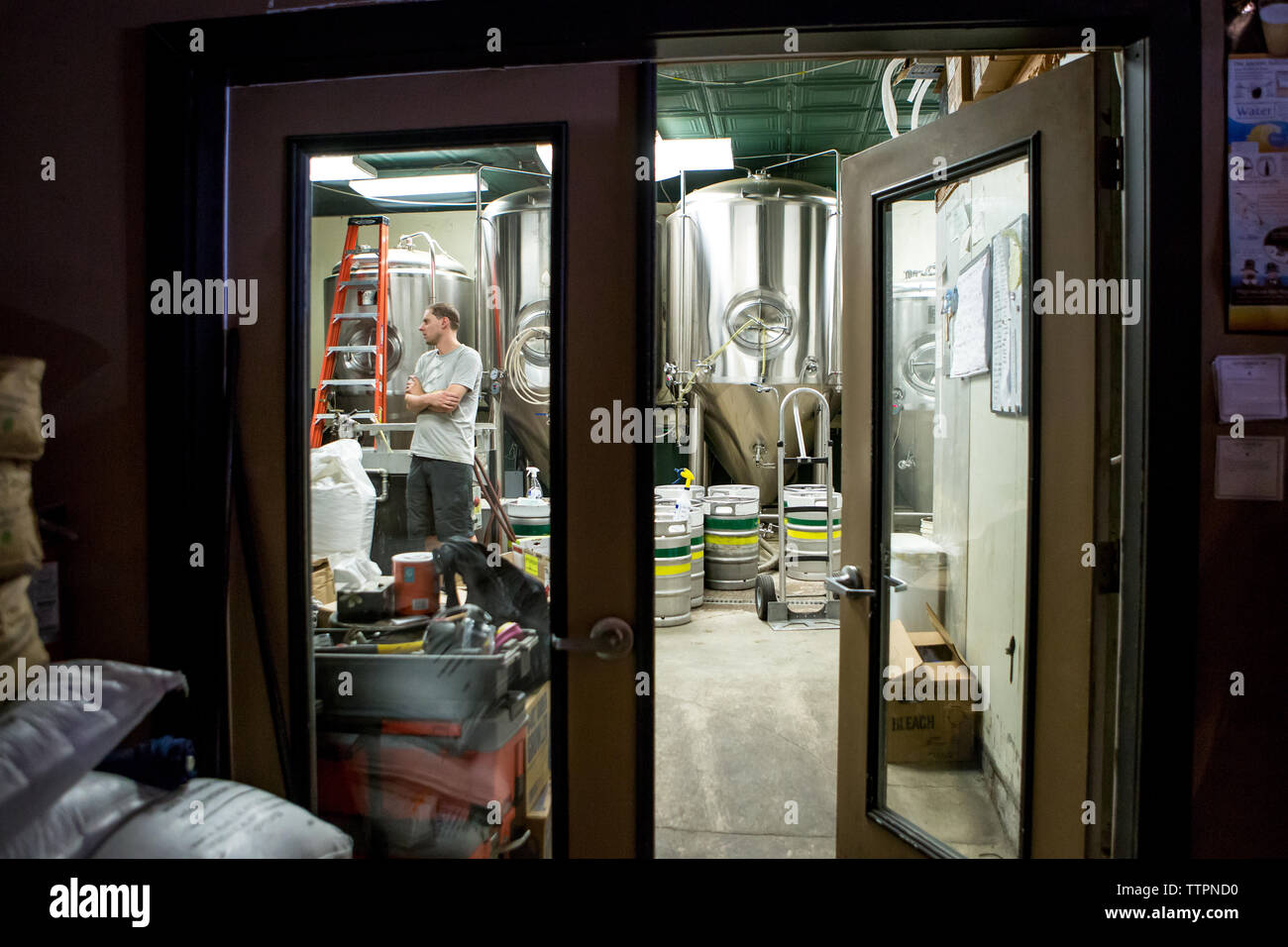 Brewery worker with arms crossed standing contre les cuves de fermentation Banque D'Images