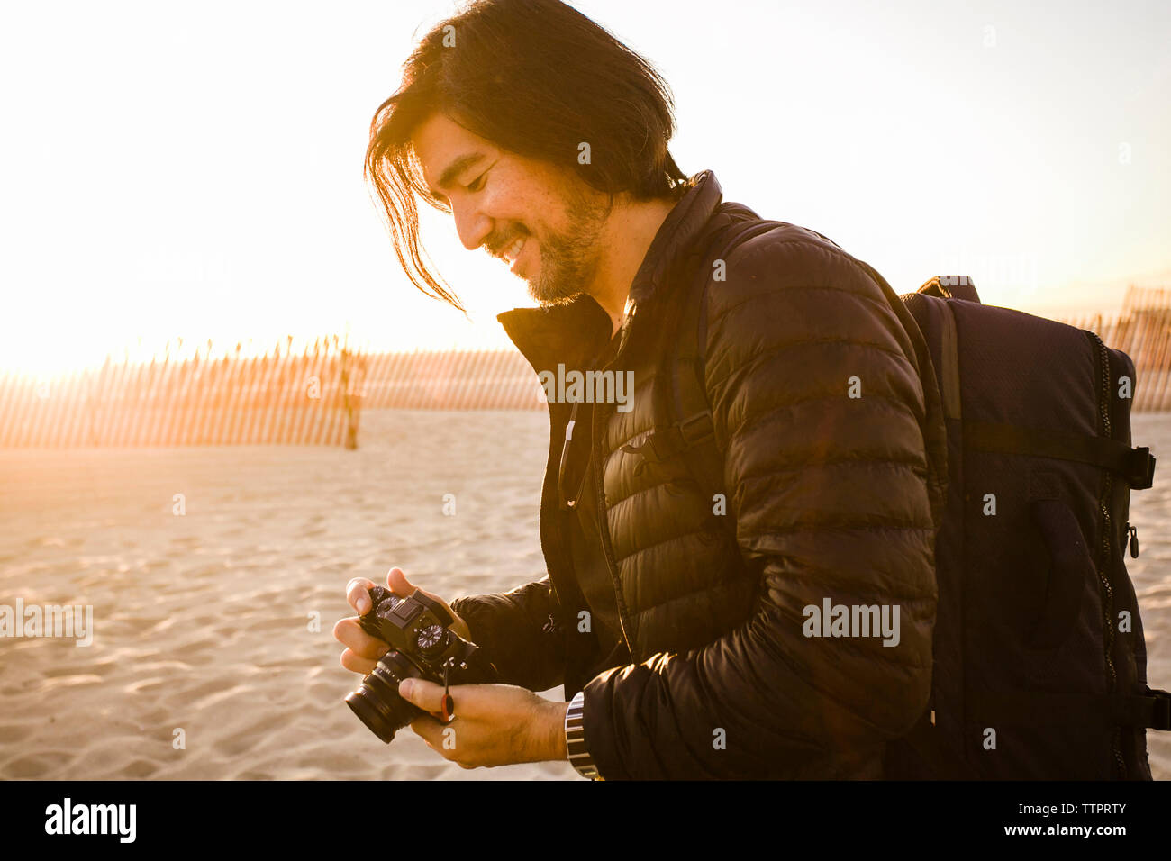 Vue de côté de l'homme souriant avec sac à dos et appareil photo à permanent beach Banque D'Images