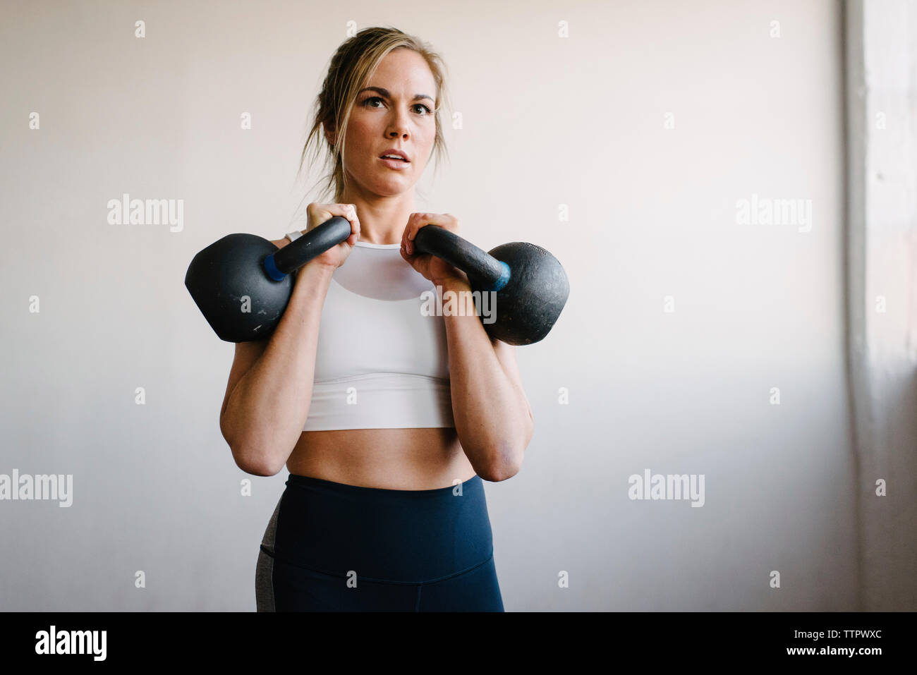 Portrait de l'athlète féminine en position debout par kettlebells wall in gym Banque D'Images