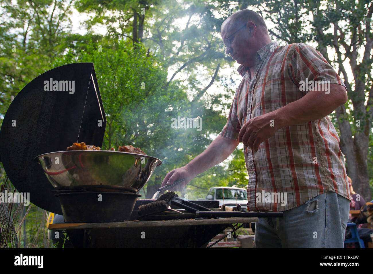 Low angle view of man de la cuisson du poulet sur la grille du barbecue en forêt Banque D'Images