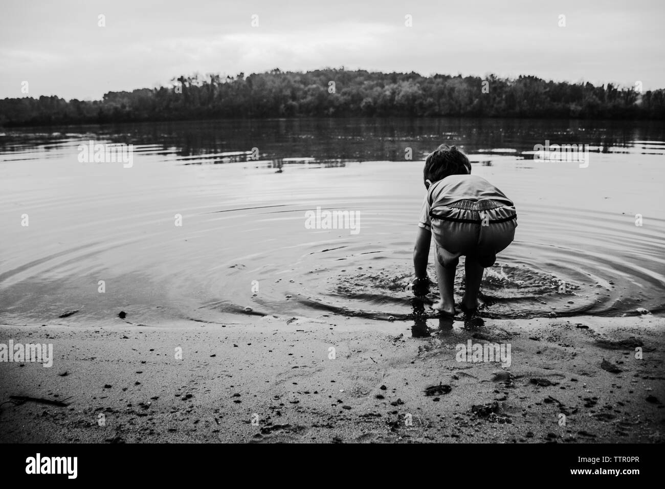 Garçon de rincer les mains sur le bord d'un lac créer ripples Banque D'Images