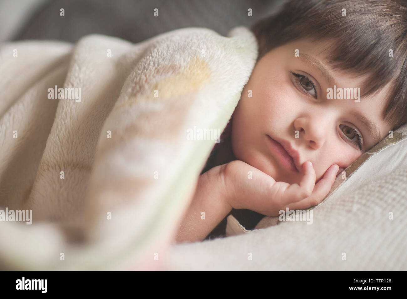 Close-up portrait of boy lying in bed at home Banque D'Images