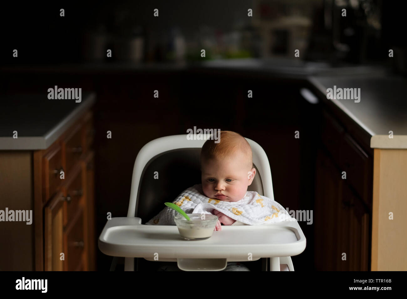 Baby Boy looking at food dans un bol alors qu'il était assis sur la chaise haute Banque D'Images