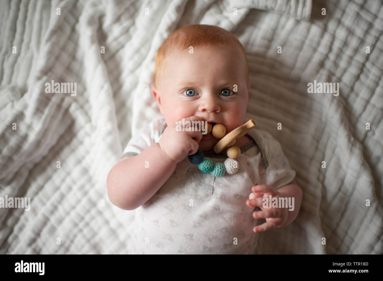 Overhead portrait of cute baby boy biting jouet en lying on bed Banque D'Images