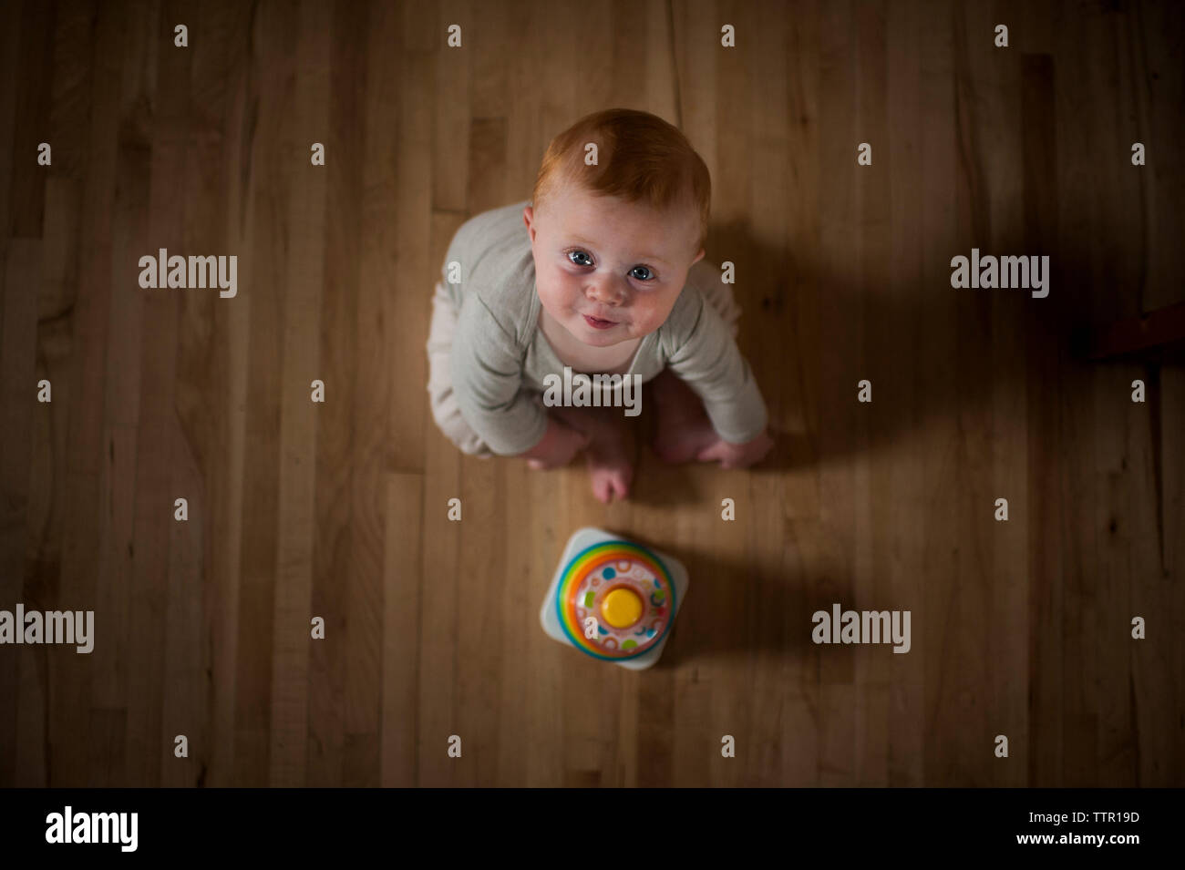 Overhead portrait of cute baby boy with toy assis sur le plancher à la maison Banque D'Images