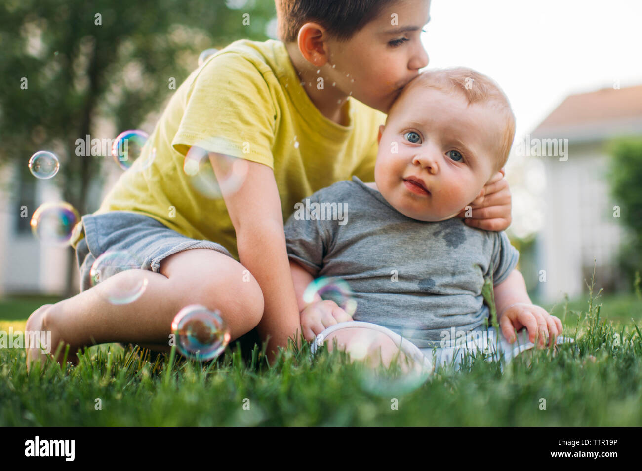 Boy kissing frère alors qu'il était assis sur les champs à l'arrière-cour Banque D'Images