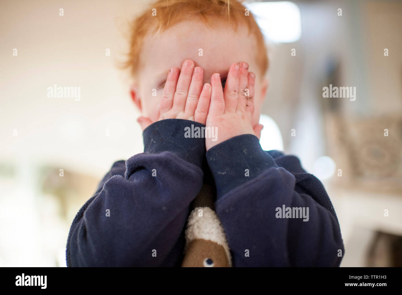 Cute baby boy hiding face tout en jouant à cache-cache à la maison Banque D'Images