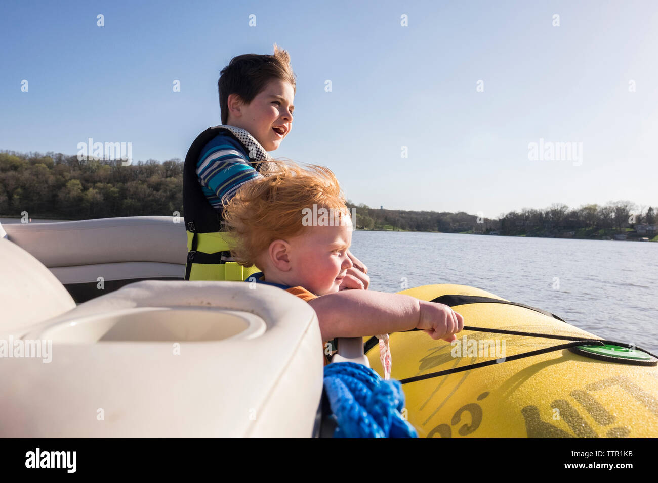 Frères portant des gilets en position debout en bateau sur le lac contre le ciel clair au cours de journée ensoleillée Banque D'Images