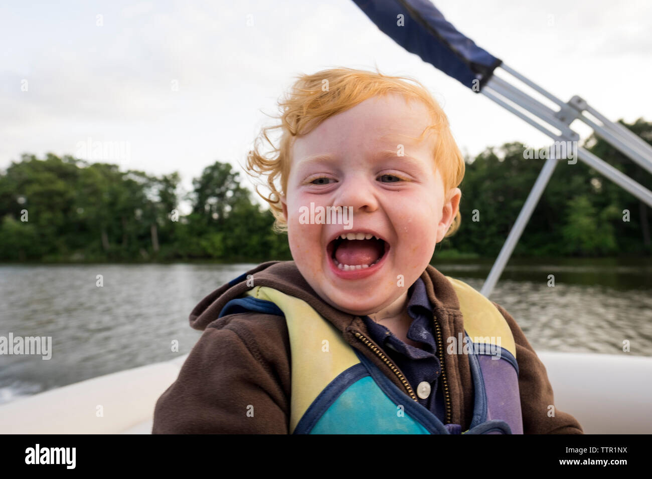 Happy cute baby boy sitting on boat in lake forest Banque D'Images
