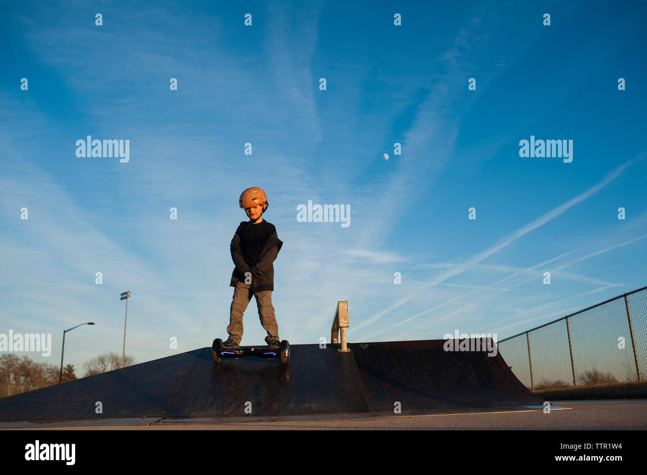 Petit garçon descente rampe de skate park contre le ciel bleu Banque D'Images