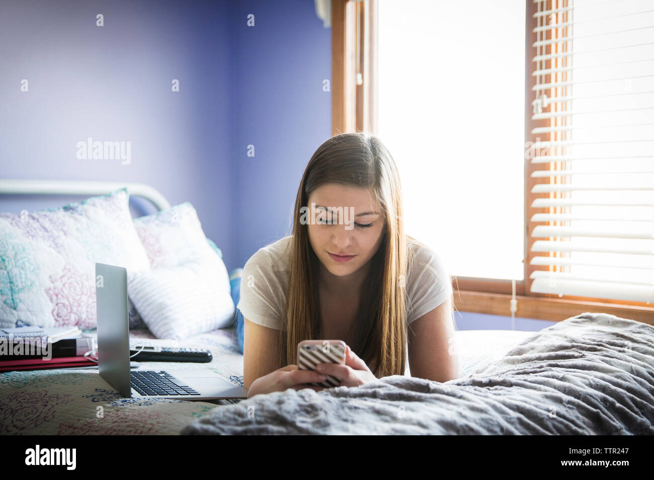 Girl en utilisant votre téléphone lorsque couché sur lit dans une chambre bien éclairée Banque D'Images