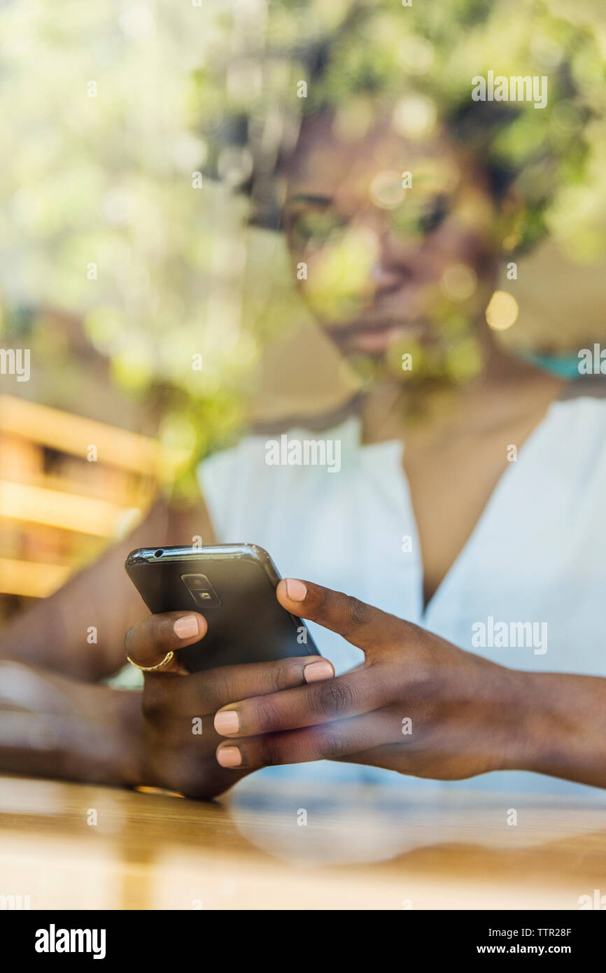 Femme à l'aide de smart phone vu à travers la fenêtre de verre en magasin Banque D'Images