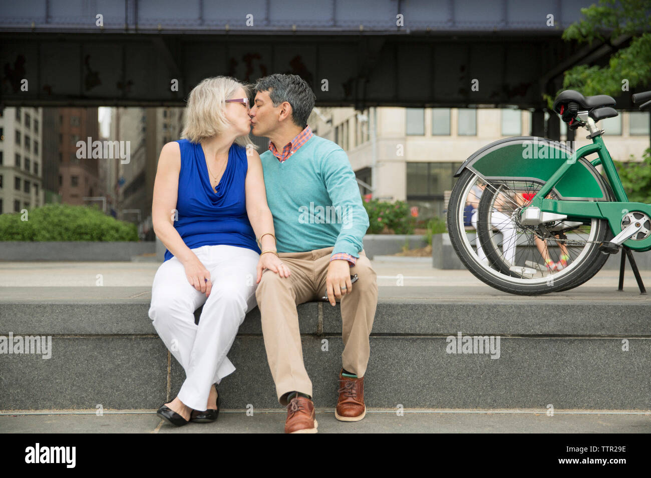 Mature couple kissing while sitting on steps in city Banque D'Images