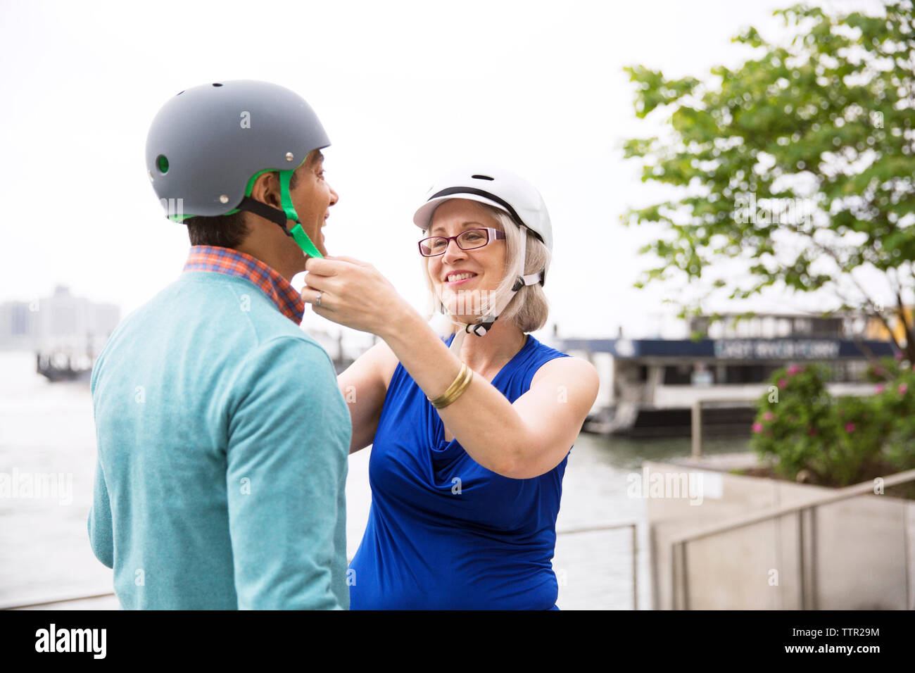 Femme mature d'aider l'homme dans le port de casque de vélo contre le ciel clair Banque D'Images