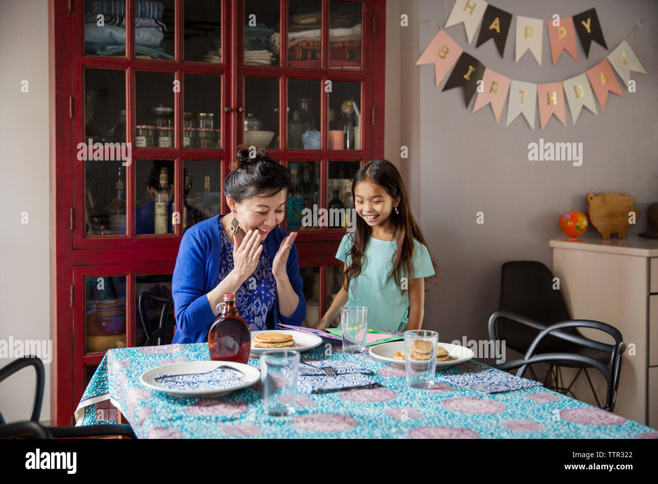 Surpris mère regardant crêpes faites par fille sur anniversaire Banque D'Images