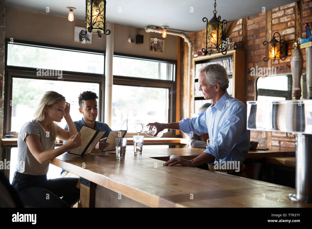 Propriétaire servant des boissons aux clients au comptoir de cafe Banque D'Images