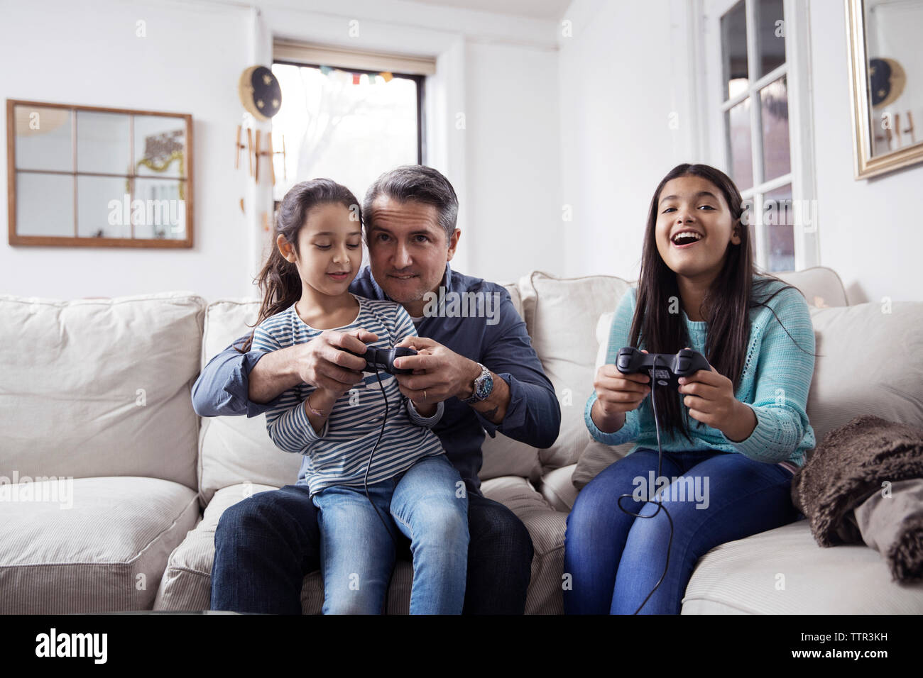 Les filles avec le père playing video game while sitting on sofa at home Banque D'Images