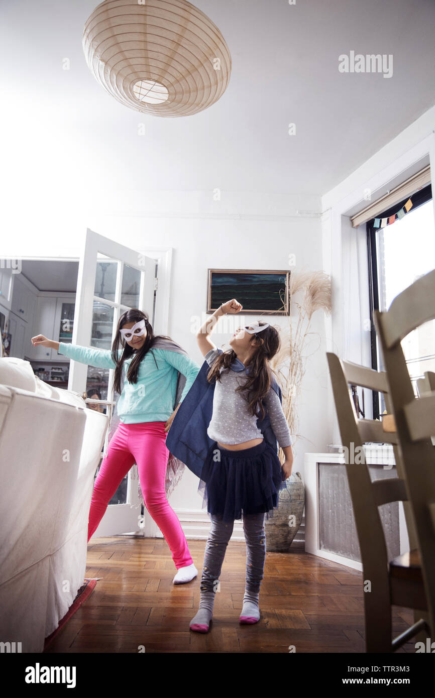 Porter des lunettes de filles enjouées des masques et des capes en se tenant à la maison Banque D'Images