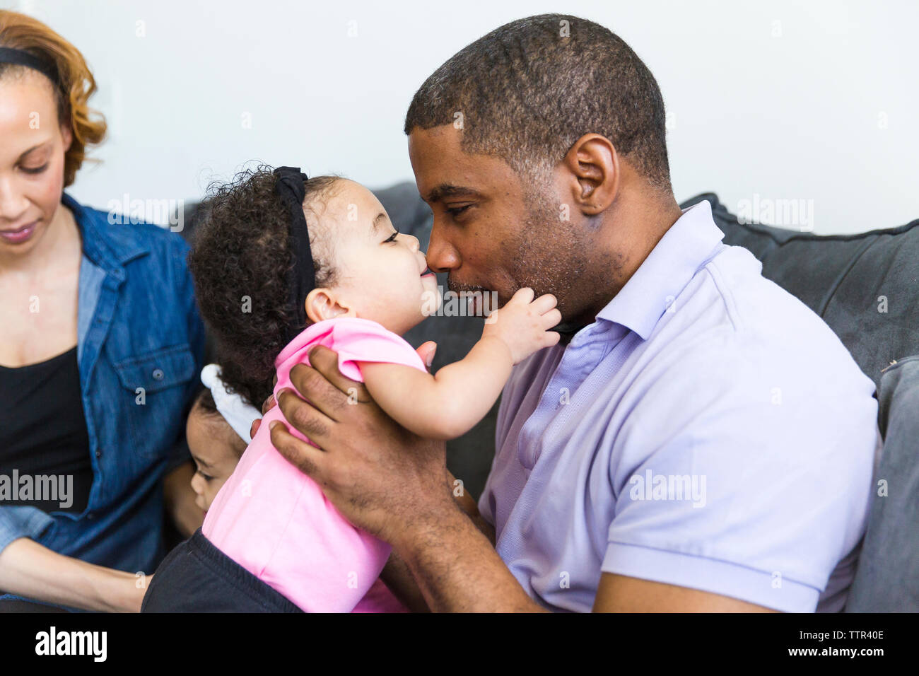 Petite fille jouant avec le père avec la mère et la soeur assis en arrière-plan Banque D'Images