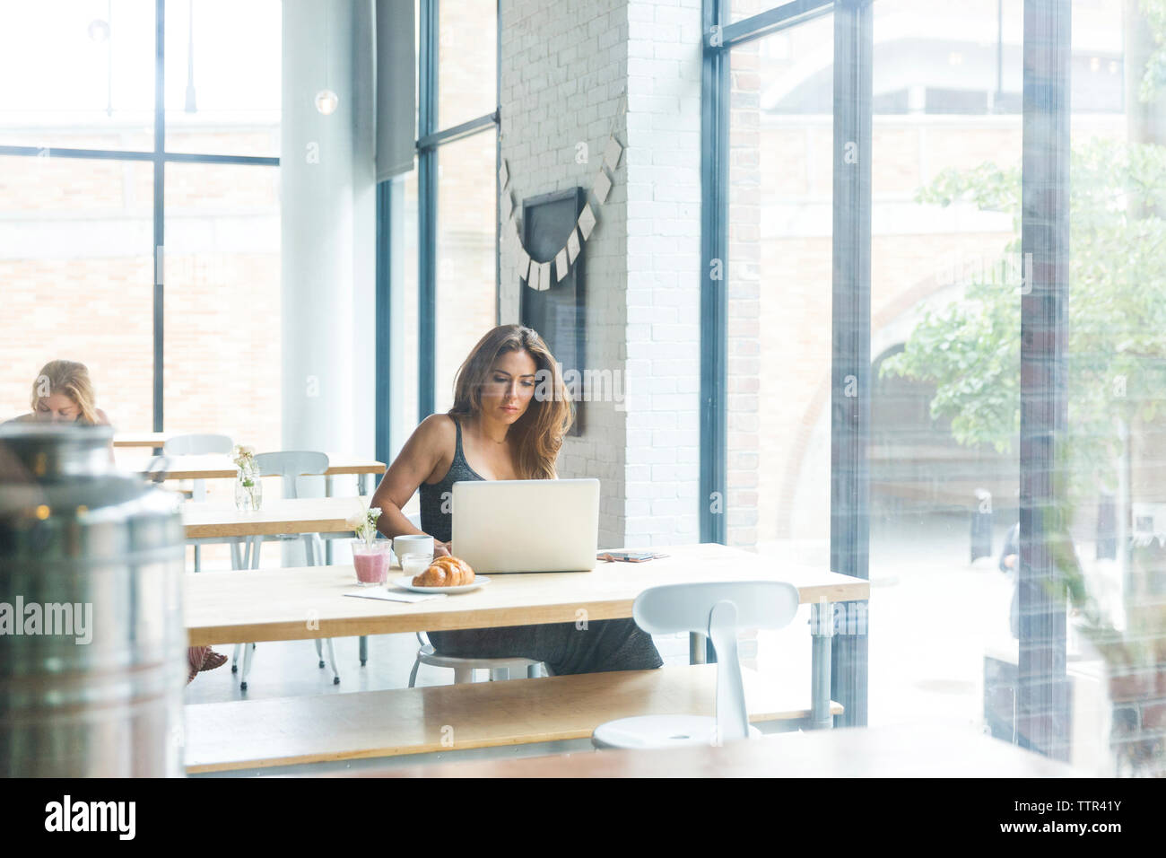 Woman while sitting in cafe avec ami en arrière-plan de la fenêtre vu par Banque D'Images