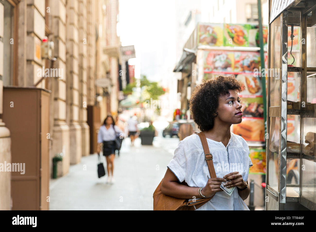 Thoughtful woman holding monnaie de papier tout en se tenant au magasin en ville Banque D'Images