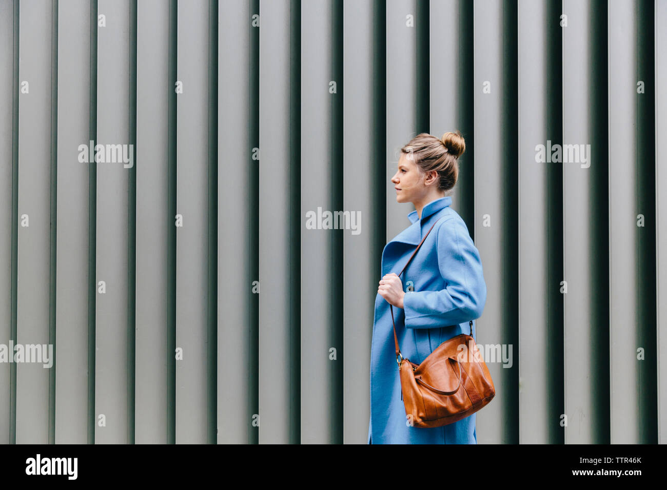 Side view of young woman wearing trench coat en portant votre sac à main contre shutter en ville Banque D'Images